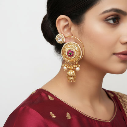 Gold earrings with intricate design and pearl and gemstone accents on a person's ear.